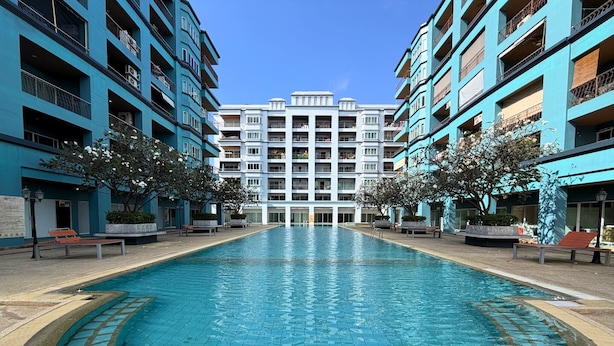 Ein Pool mit einer gefliesten Kante, umgeben von einem Gebäude mit mehreren Balkonen und blauem Himmel.