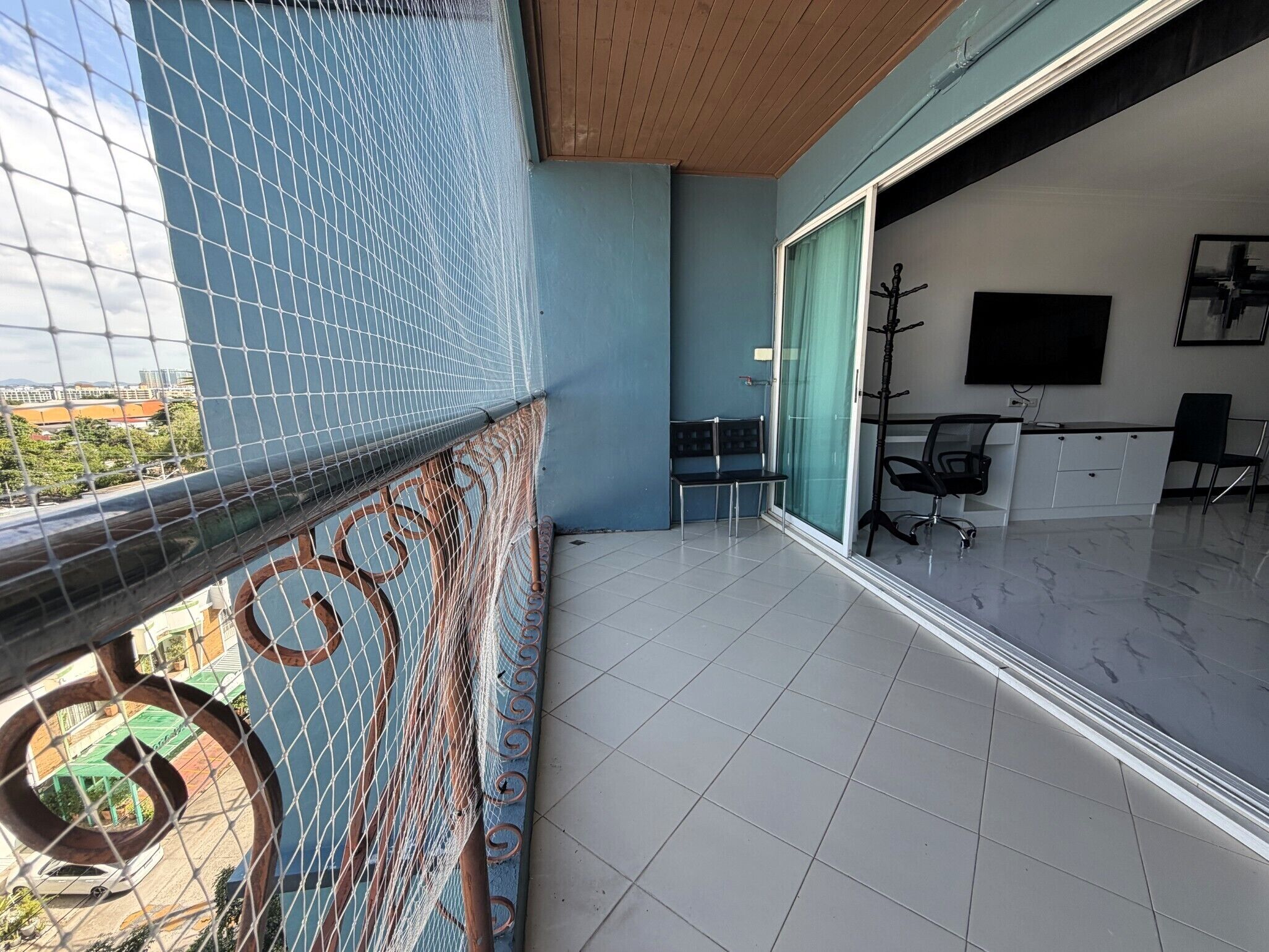 Een balkon met uitzicht op de stad, een bureau met stoel, en een aan de muur bevestigde televisie.