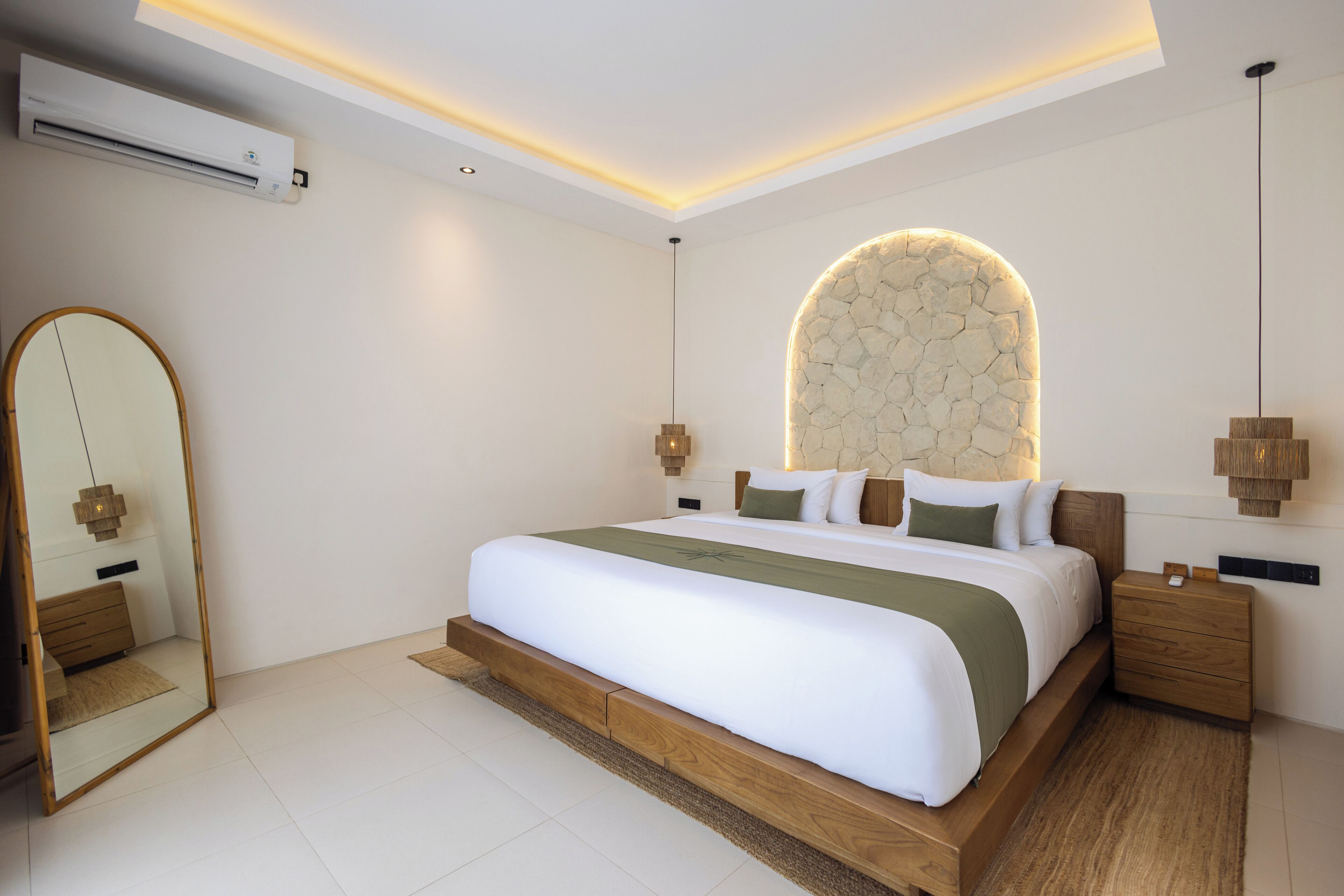 A modern bedroom with a large bed, a stone accent wall, and a mirror.