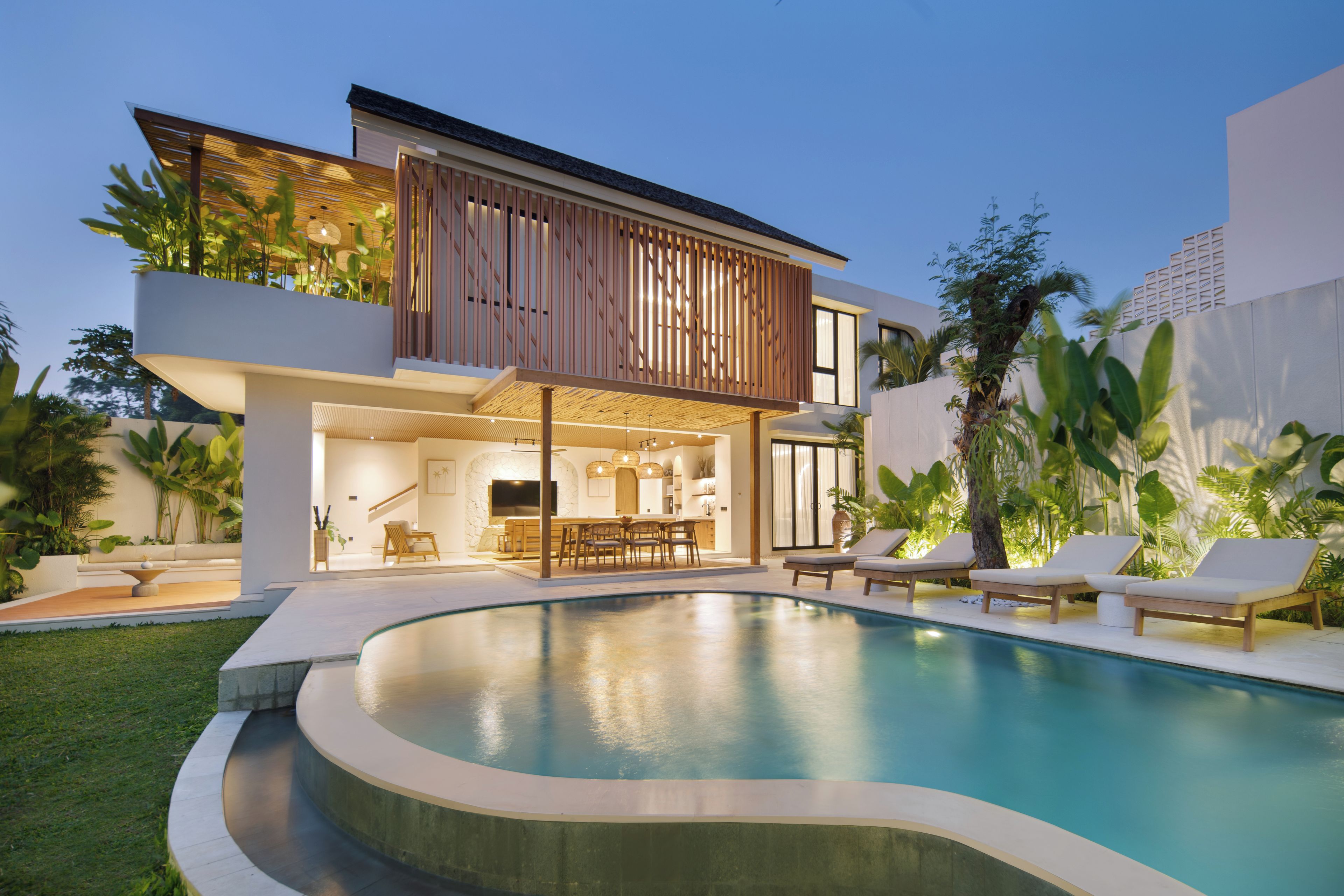 A modern two-story house with a swimming pool, outdoor seating, and tropical plants.