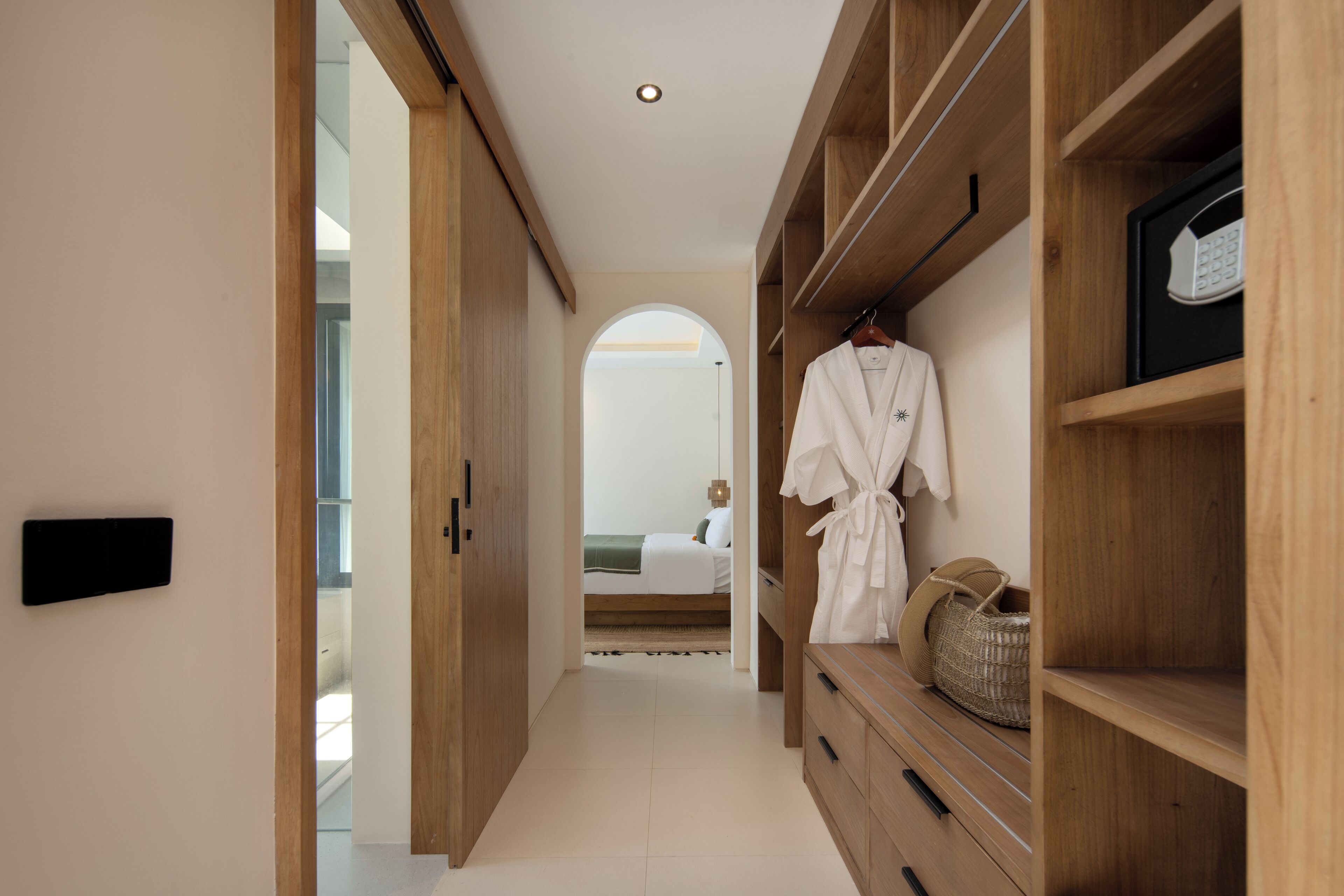 A hallway with wooden shelving, a robe hanging, and a basket on the right.