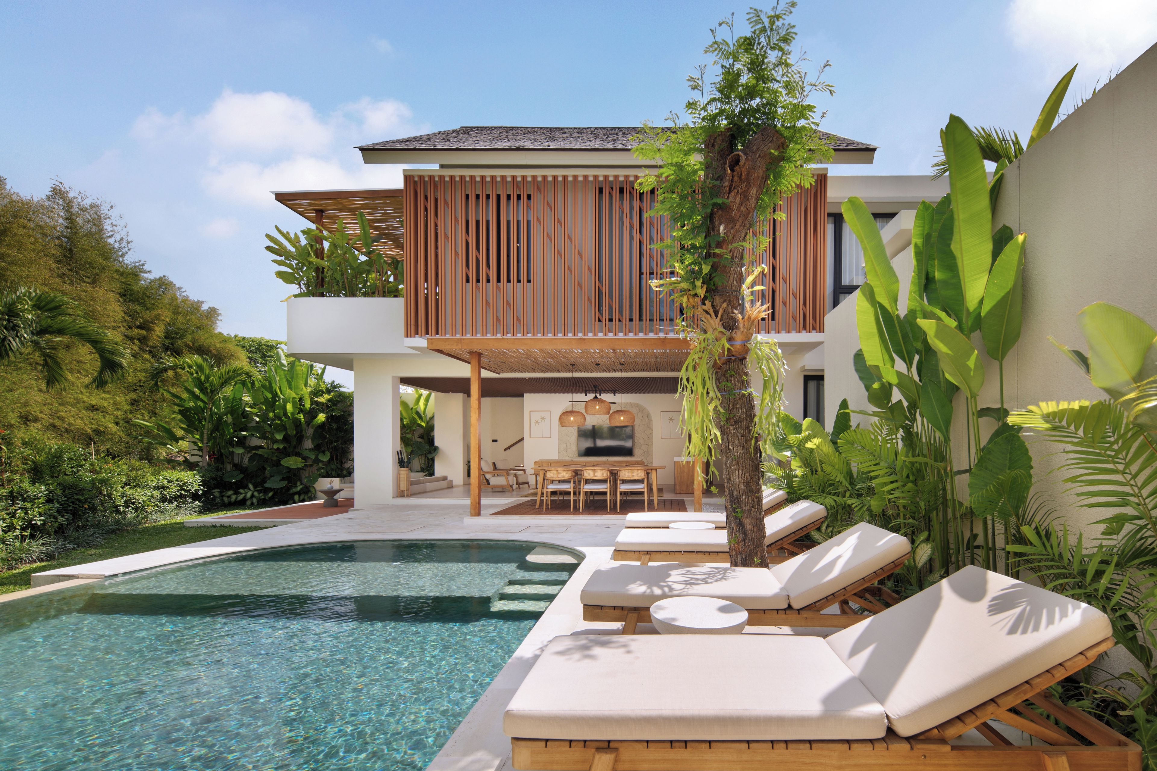 A modern poolside area with a clear pool, lounge chairs, and a dining area.