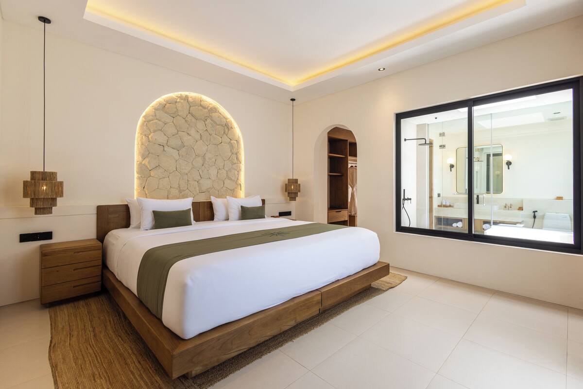 Une chambre moderne dotée d’un grand lit, d’une arche en pierre, d’un dressing et d’une grande fenêtre donnant sur la salle de bain.