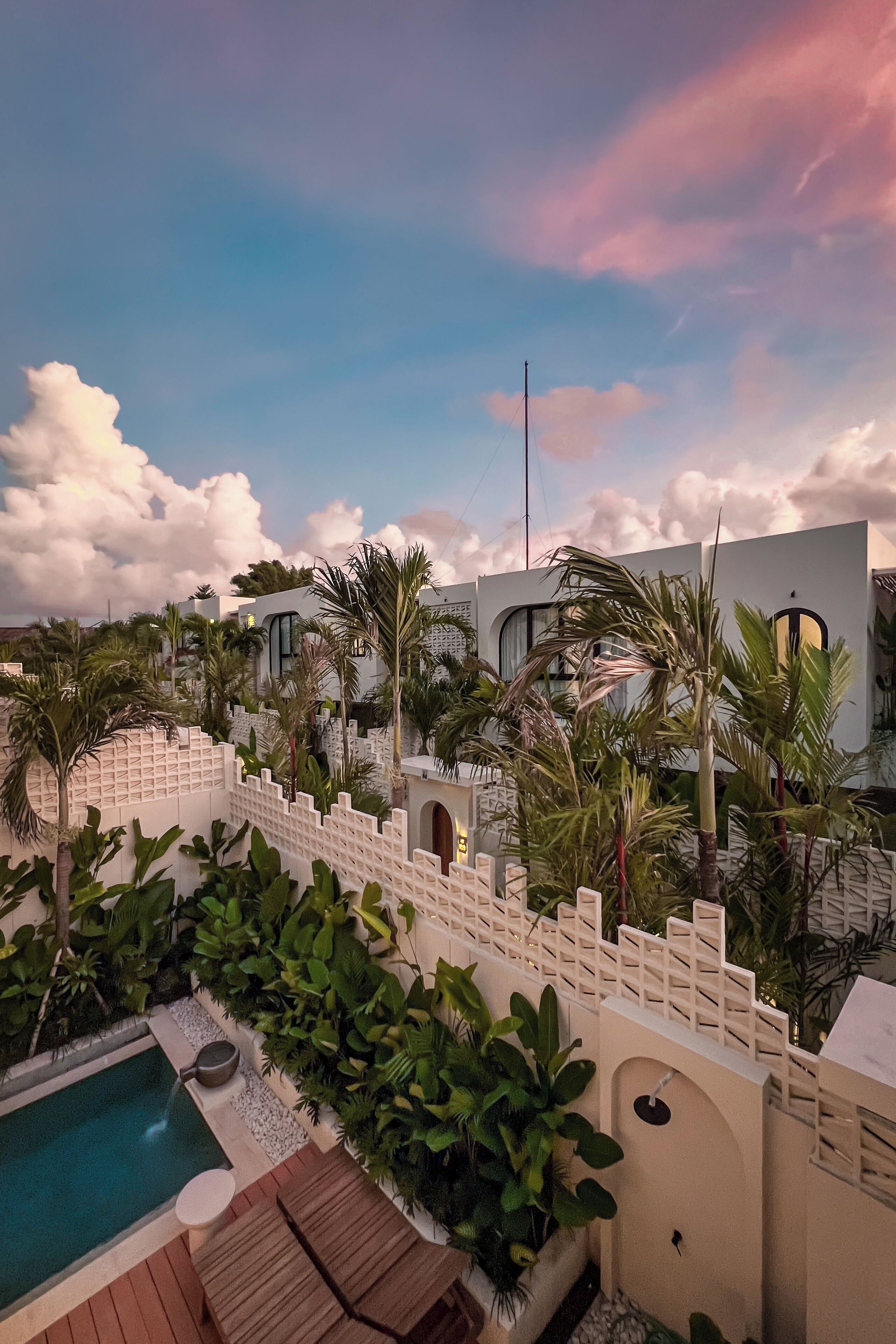 A pool area with a wooden deck and a small pool, surrounded by lush greenery and palm trees.