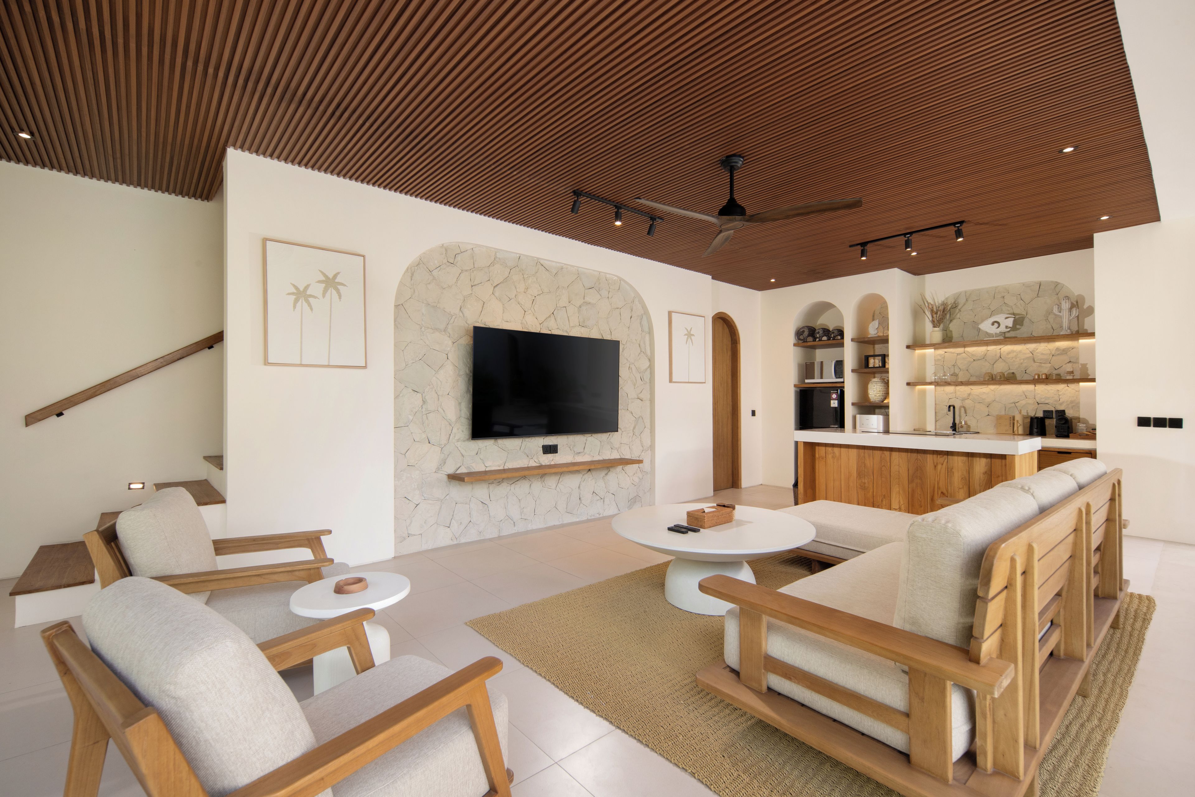 A modern living room with a flat-screen TV, comfortable seating, and a kitchen area with a bar.