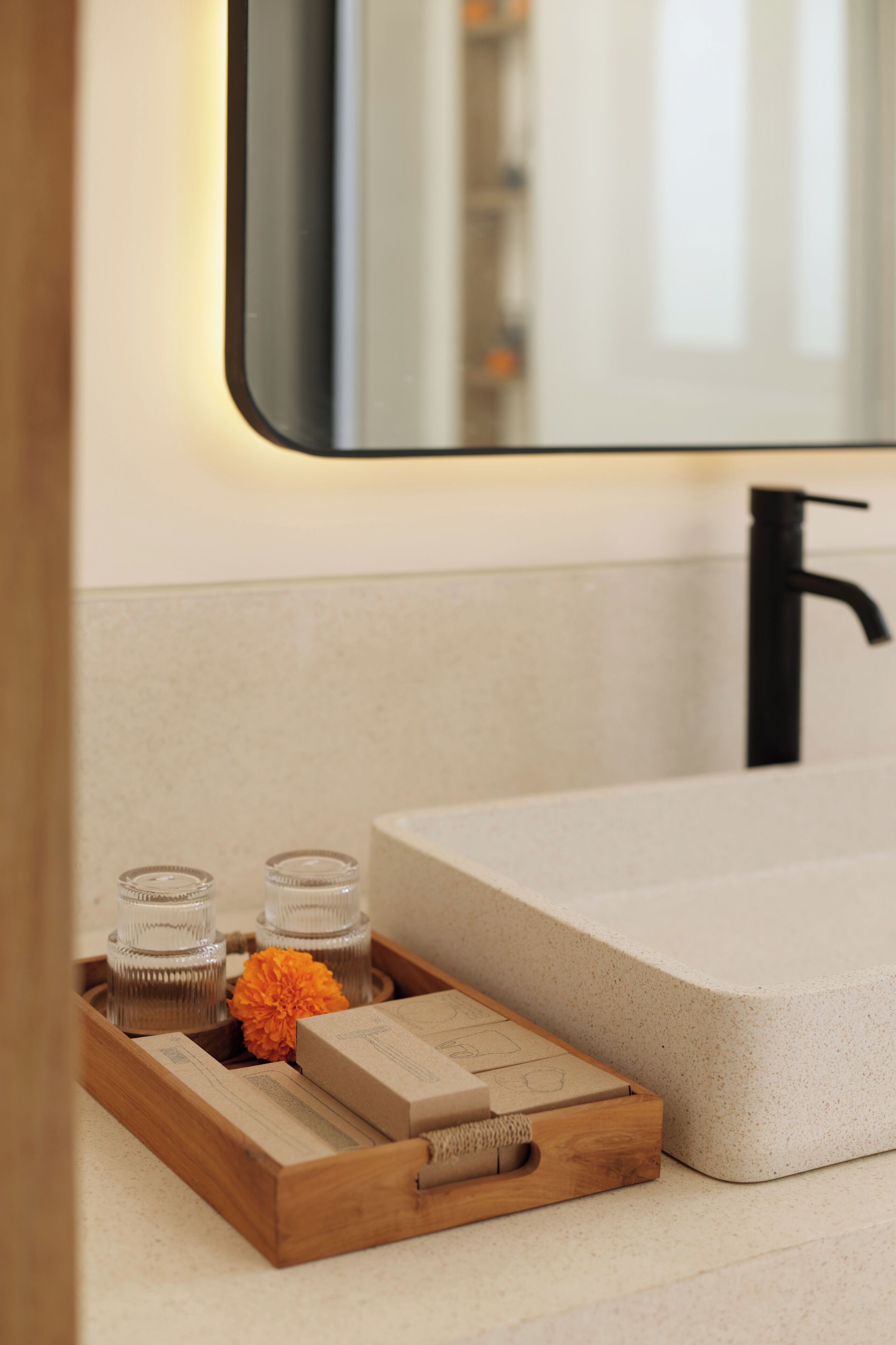 Un bagno con un vassoio di legno con candele e un fiore, un lavandino e uno specchio.