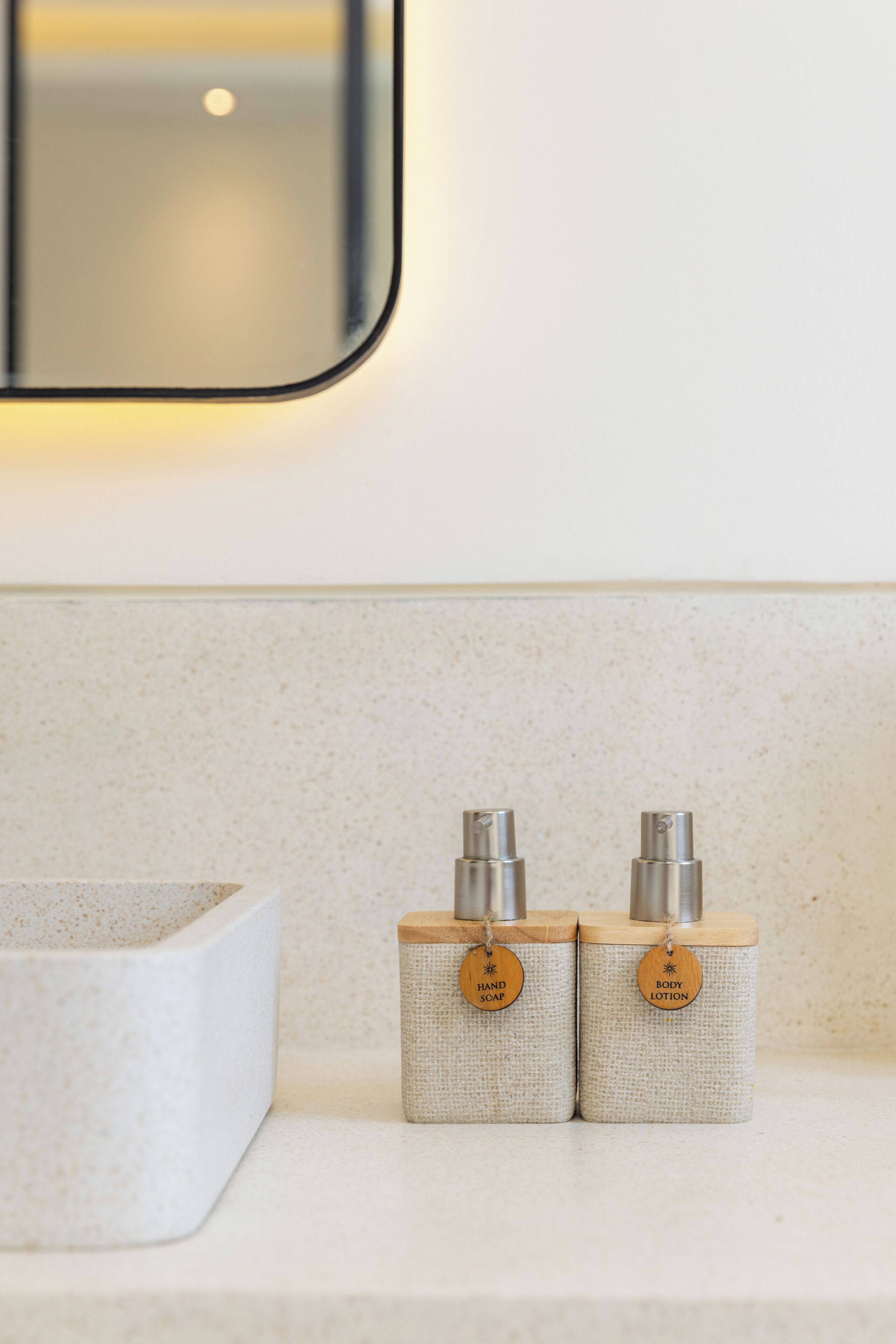 A bathroom with a white sink and two soap dispensers labeled "HAND SOAP" and "BODY LOTION" on a speckled beige countertop.