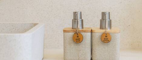 A bathroom with a white sink and two soap dispensers labeled "HAND SOAP" and "BODY LOTION" on a speckled beige countertop.