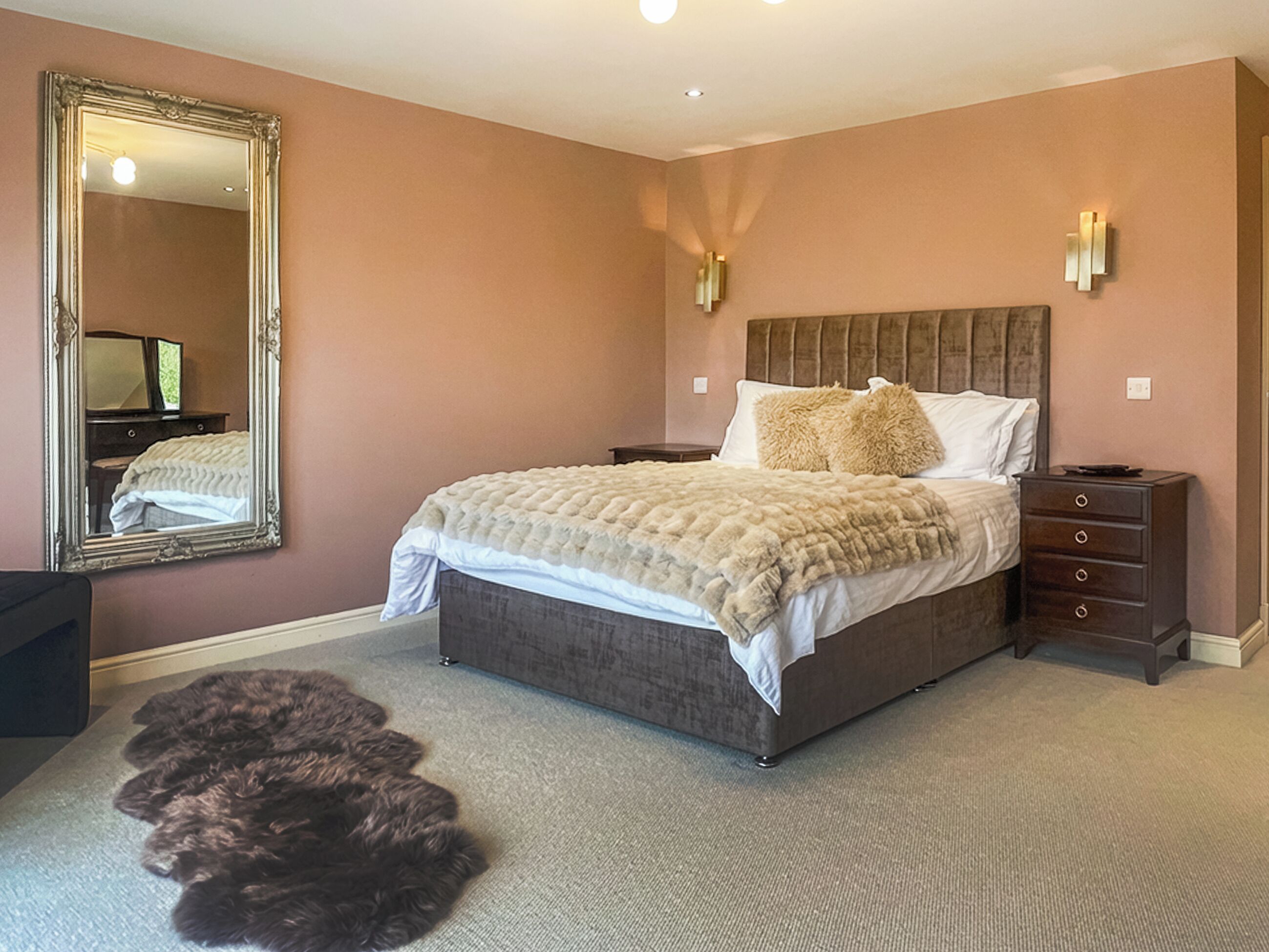 Ein Schlafzimmer mit einem großen Bett, einem Schminktisch, einem Spiegel und einem flauschigen Teppich.