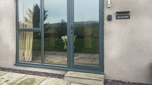 Entrada de un edificio moderno con puerta corredera de vidrio, una placa que dice “The Fox Hole” y un pequeño espacio exterior con un camino de grava y una maceta.