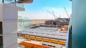 Un edificio moderno con fachada de vidrio, una azotea con paneles solares y grúas de construcción al fondo.