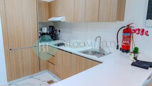 Una cocina moderna con armarios de madera, encimera blanca, pileta de acero inoxidable, máquina de café y extintor.