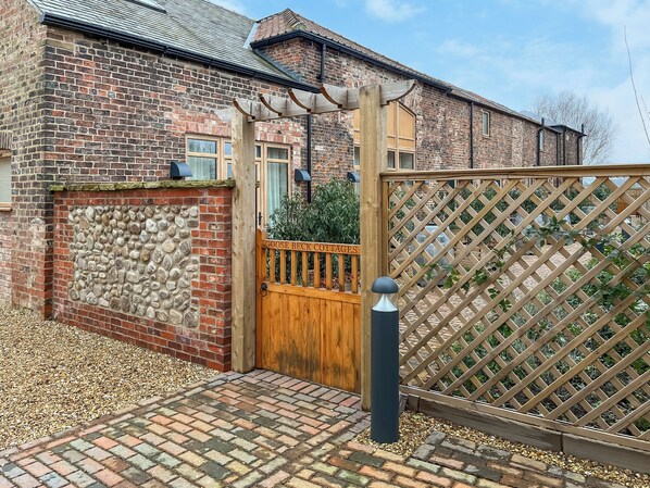 A brick cottage with a stone wall, wooden gate, and a lattice fence.