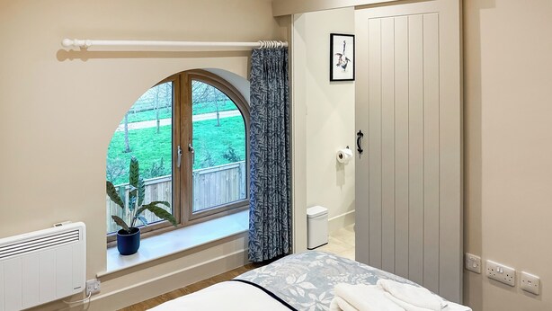 Ein Schlafzimmer mit Bett, Fenster mit Blick auf eine grüne Landschaft, Heizkörper und Tür.