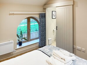 A bedroom with a bed, a window with a view of a green landscape, a radiator, and a door.