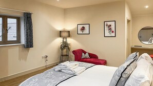Una camera da letto con un letto, una poltrona rossa, una lampada da terra e due quadri floreali appesi al muro.