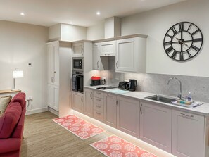 A modern kitchen with white cabinets, a black clock, and a red patterned rug. - Goose Beck Cottages - Rondo (Tockwith, near York)