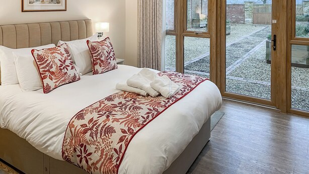 Ein Schlafzimmer mit einem großen Bett, einem Kopfteil, einem Nachttisch mit Lampe und einem Fenster mit Vorhängen.
