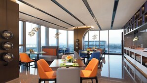 A modern dining area with a high ceiling, large windows, and a view of a bridge. - Hampton by Hilton Hangzhou Xiaoshan Jiangnan Technology City. (Hangzhou)