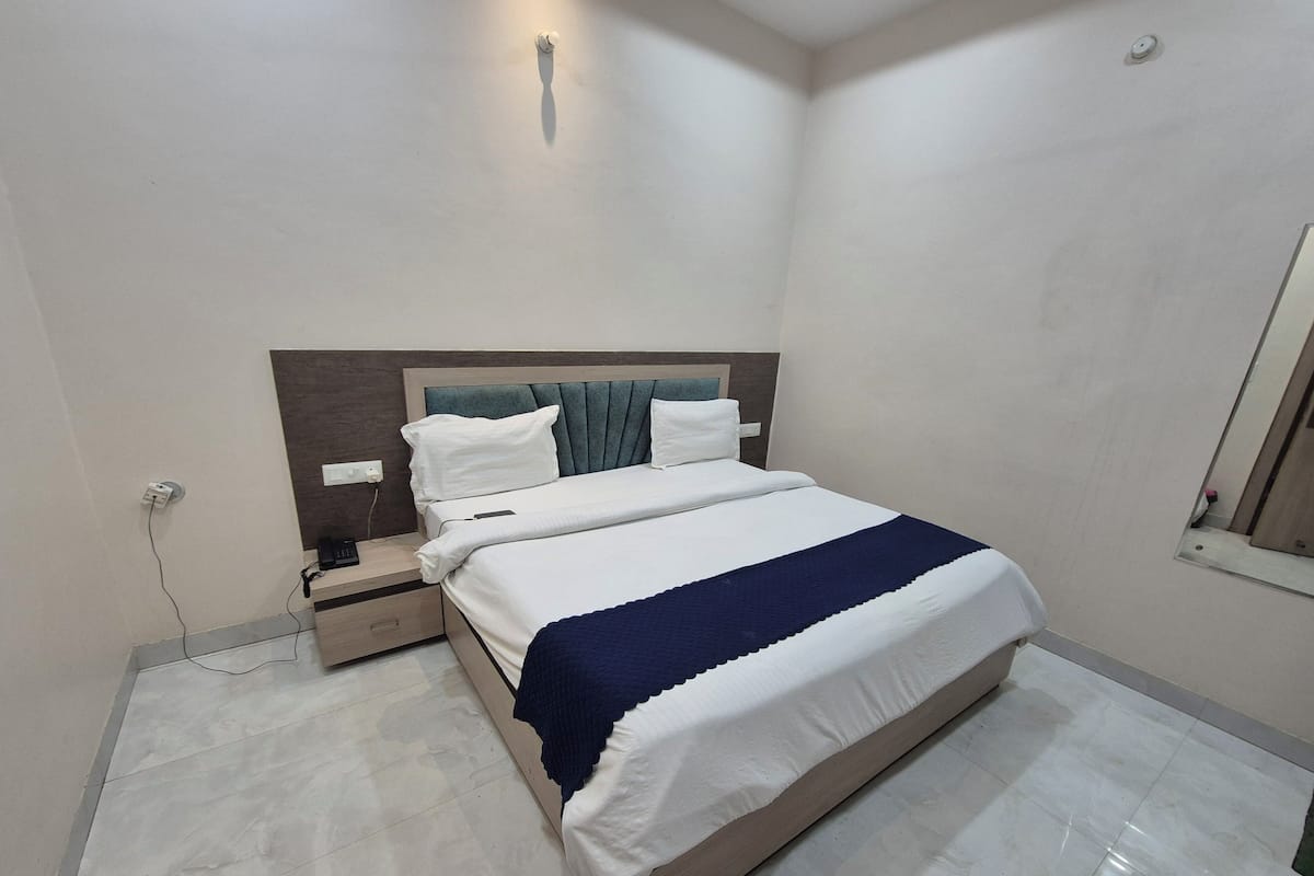 Una cama bien hecha con un edredón azul, una mesita de noche con un teléfono y un enchufe de pared.