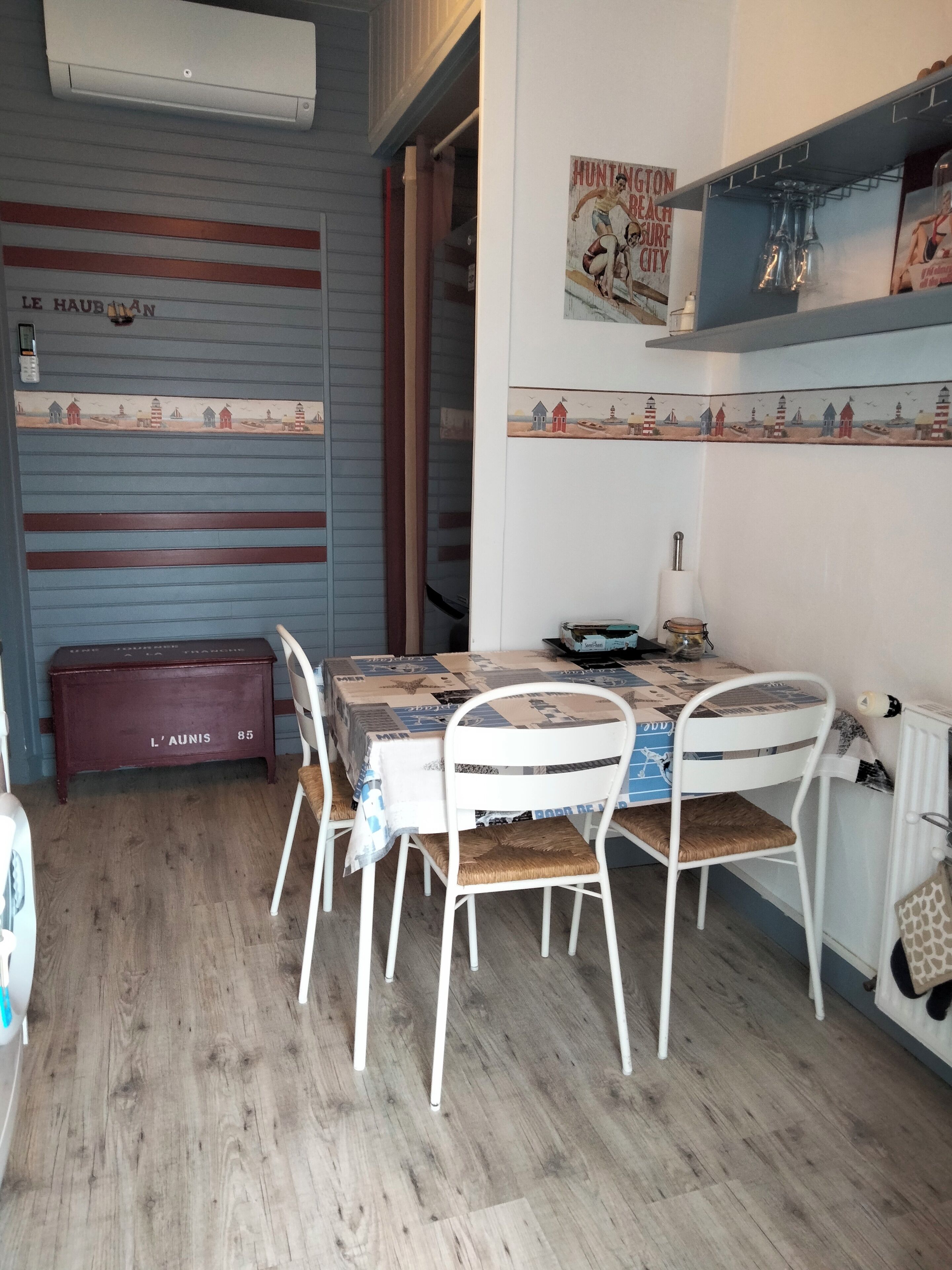 A dining area with a table set for four, white chairs, a red bench, and a wall with a nautical-themed mural.