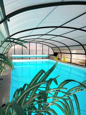 A covered swimming pool with a curved roof structure, surrounded by potted plants. - Gîte le Hauban, with covered swimming pool. Near town center and beach (La Tranche-sur-Mer)