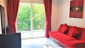 Un sofá rojo con almohadones, un televisor y un balcón con cortinas rojas.