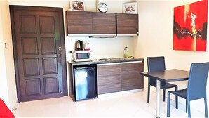 Una cocina compacta con microondas, pileta y un refrigerador pequeño. Hay una mesa de comedor con sillas y un cuadro abstracto rojo en la pared.