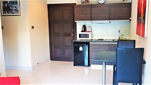 Una cocina compacta con armarios de madera oscura, un microondas, un refrigerador pequeño y una mesa de comedor con sillas.
