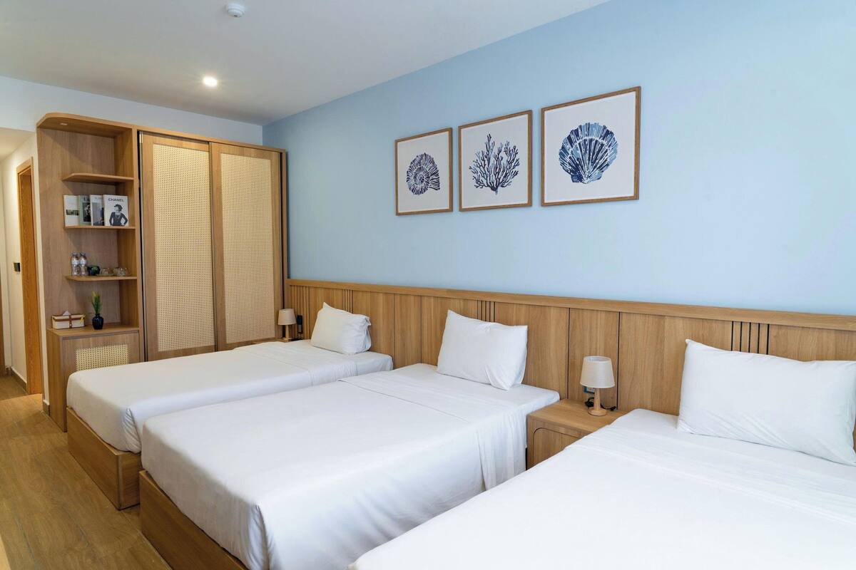 A hotel room with two beds, a wooden wardrobe, and three framed pictures on the wall.