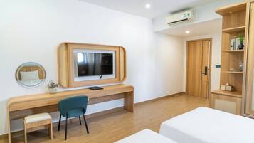 A modern hotel room with a wooden desk, a television, a small chair, a bed, and a wardrobe.