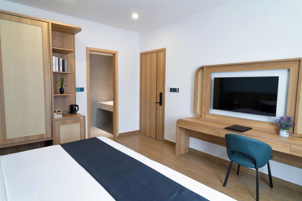 A modern hotel room with a bed, a desk with a chair, a TV, and a wardrobe.
