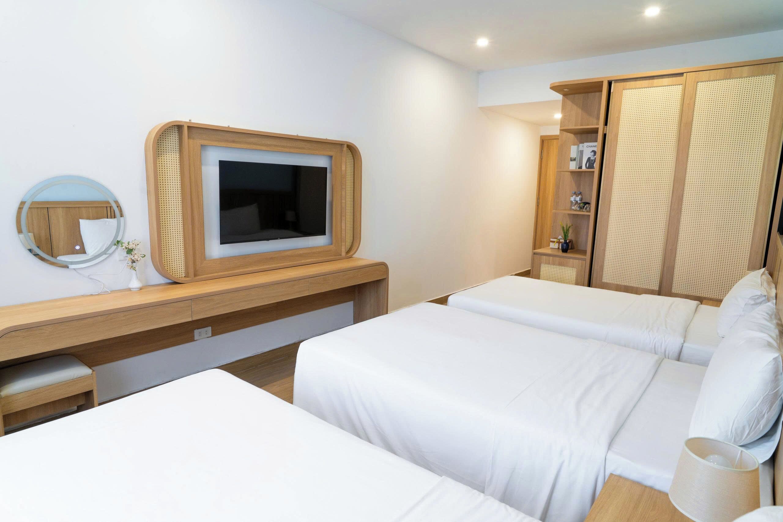 A hotel room with a wooden desk, a television, a wardrobe, and two beds.