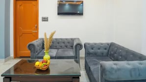 A living room with two grey sofas, a wooden door, a flat-screen TV mounted on the wall, and a glass coffee table with a fruit basket. - OnlyStay River Pine Kasol (Sosan)