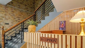 A reception area with a wooden reception desk, a sign reading "RECEPTION," a staircase with a metal railing, and a potted plant. - OnlyStay River Pine Kasol (Sosan)