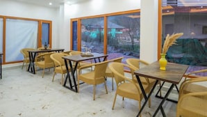 A dining area with tables and chairs, large windows with a view, and a ceiling fan. - OnlyStay River Pine Kasol (Sosan)