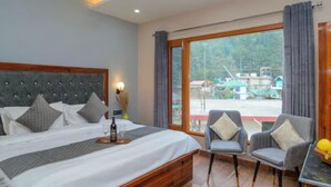 A bedroom with a large bed, two armchairs, a small table, and a view of the outside. - OnlyStay River Pine Kasol (Sosan)
