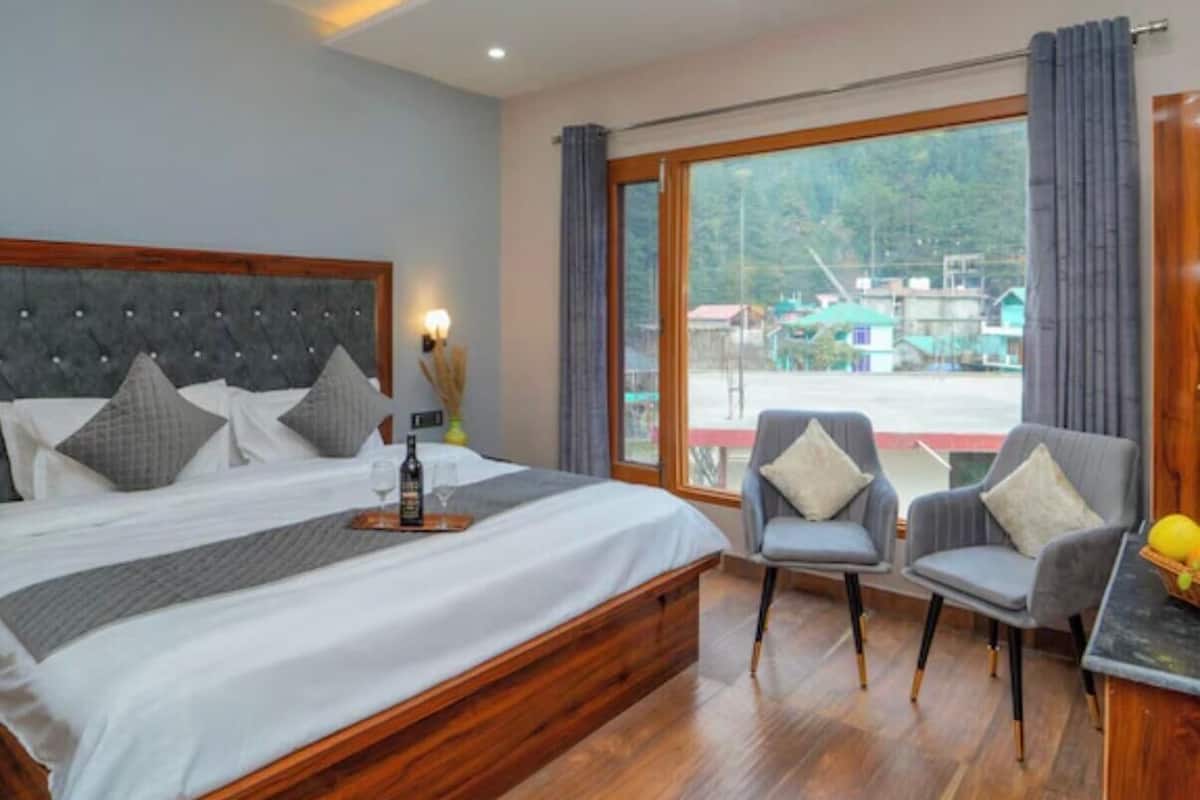 A bedroom with a large bed, two armchairs, a small table, and a view of the outside.