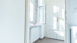 Un couloir lumineux aux murs blancs, avec un radiateur et une porte dotée d’une poignée dorée.