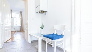 Une chaise blanche avec un coussin bleu, placée dans un couloir lumineux aux murs blancs et au sol carrelé.