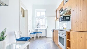 Une cuisine compacte avec des meubles en bois, un plan de travail blanc et une fenêtre qui laisse entrer la lumière naturelle.