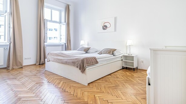 Une chambre à coucher avec un grand lit, deux tables de chevet, un radiateur et une fenêtre avec des rideaux.
