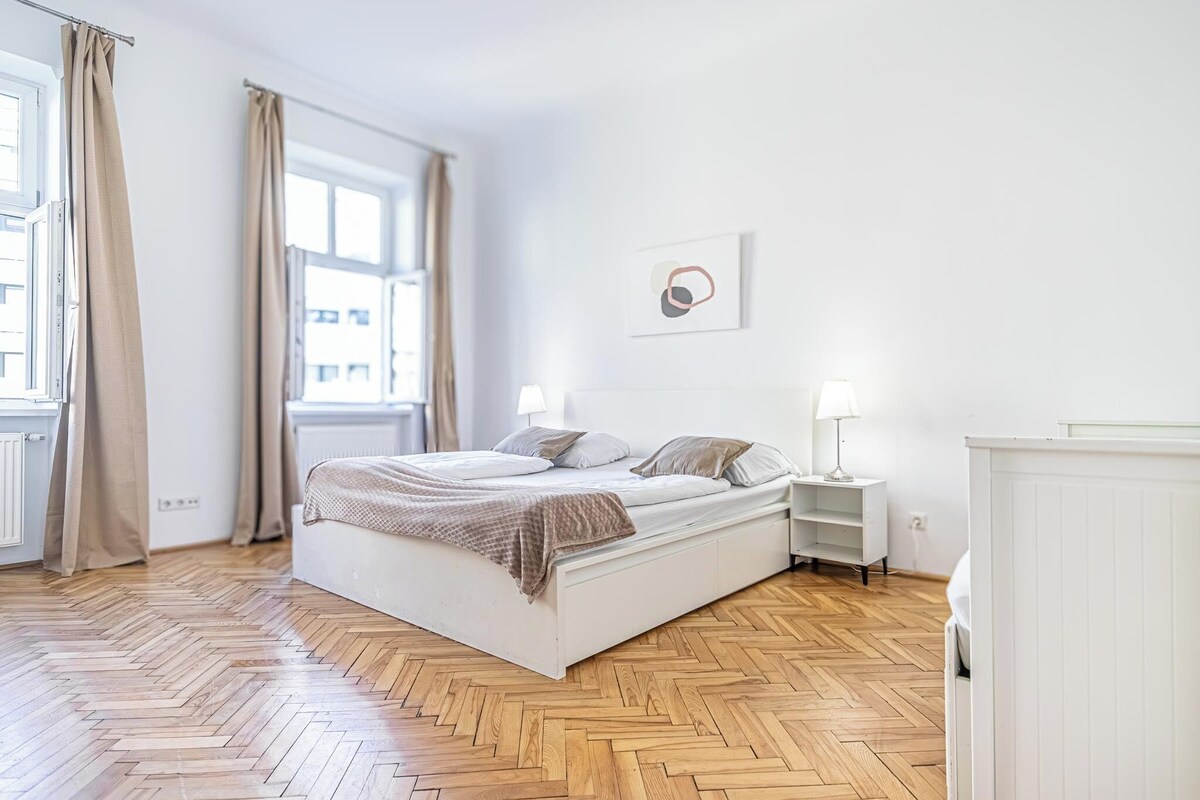 Ein Schlafzimmer mit einem großen Bett, zwei Nachttischen, einem Heizkörper und einem Fenster mit Vorhängen.