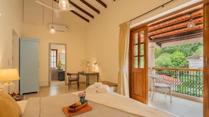 A hotel room with a bed, a desk, a chair, and a balcony with a view of greenery. - ELIVAAS Celest 4 BHK Villa with Pvt Pool (Arpora)