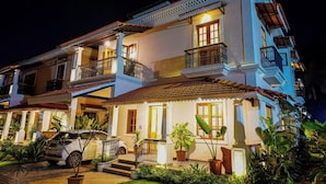 A multi-story building with balconies, a car parked in front, and potted plants around the entrance. - ELIVAAS Celest 4 BHK Villa with Pvt Pool (Arpora)