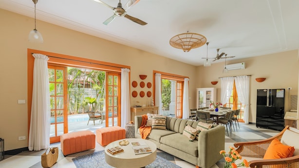 A spacious living area with a sofa, ottoman, and coffee table, a dining area, and a kitchen. - ELIVAAS Celest 4 BHK Villa with Pvt Pool (Arpora)