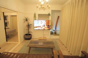 A living room with a television, a chandelier, a potted plant, and a wooden bench.