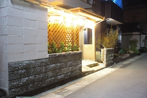 A residential building with a stone facade, a wooden lattice door, and a small porch area with steps leading to the entrance.
