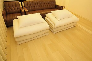 A brown leather sofa with a tufted backrest and armrests, a wooden floor, and neatly stacked white pillows.