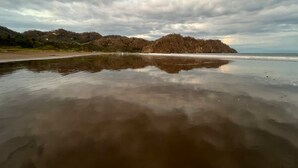 A beach with a calm water surface reflecting the sky and surrounding landscape. - Charming 3-bedroom House Rental in Paquera, Costa Rica (Paquera)